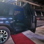 Black SUV limo with rear door open and red carpet entrance.