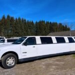 White stretch SUV limousine parked outdoors under a clear blue sky.