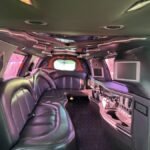 Luxurious black leather seating inside SUV limousine with dual monitors and glassware bar.