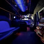 Wide-angle shot of the interior of an SUV limousine at night, featuring neon-lit ceiling panels, dual-tone leather seats, and built-in TV screens.