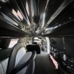 Daytime shot of a spacious SUV limo interior with plush gray and black seating, mirror-finished ceiling, and a sleek custom bar area.