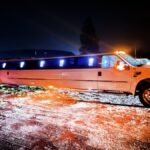 Night photo of a white Ford SUV limousine parked with blue LED lights glowing through the tinted windows and orange headlights on.