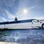 Daytime image of a stretched Ford SUV limo with black tinted windows, custom wheels, and a sleek two-tone body parked on gravel.