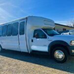 White 25-passenger party bus parked under a clear blue sky – Brantford Limo.
