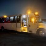 White 30-passenger party bus with entry door open and interior lights on at night – Brantford Limo.
