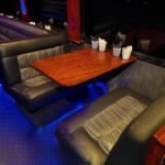 Woodgrain table seating inside 38-passenger party bus with black leather booth-style seats – Brantford Limo.