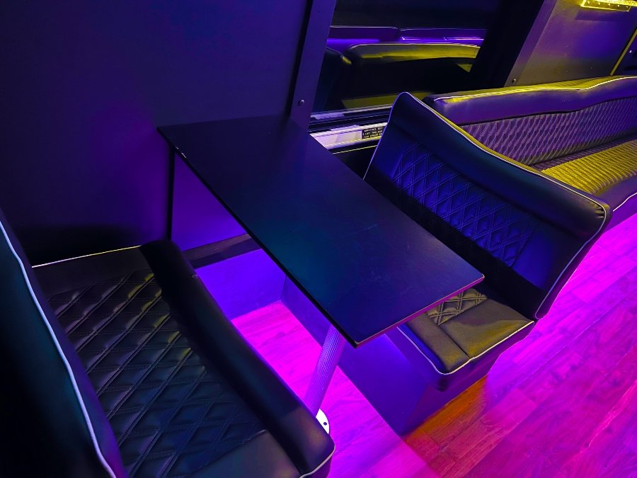 Close-up of party bus table seating with quilted leather chairs and ambient purple lighting – Brantford Limousine.